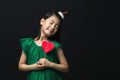 Cute asian girl child dressed in a green dress holding a Christmas ornament and a heart stick on a black background Royalty Free Stock Photo