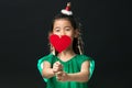 Cute asian girl child dressed in a green dress holding a Christmas ornament and a heart stick on a black background