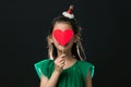 cute asian girl child dressed in a green dress holding a Christmas ornament and a heart stick on a black background Royalty Free Stock Photo