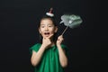Cute asian girl child dressed in a green dress holding an idea bulb stick with a christmas head decoration on a black background.