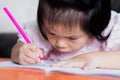 Cute Asian girl is coloring a wood color pink in a book. Child looked down at the close up.