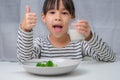 Cute Asian girl drinking a glass of milk in the morning before going to school. Little girl eats healthy vegetables and milk for