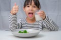 Cute Asian girl drinking a glass of milk in the morning before going to school. Little girl eats healthy vegetables and milk for