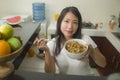 Cute Asian girl eating healthy - young beautiful and happy Korean woman at home kitchen having lunch smiling cheerful holding food Royalty Free Stock Photo