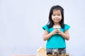 Cute Asian girl holds the lid of jar with coin and smiling looks at camera. Child put in lot of silver coins in jar.