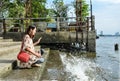 A cute Asian girl kneeling near the riverside dock