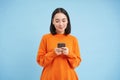 Cute asian girl looks at her cellphone and smiles, uses mobile application, social media app, playing game on phone Royalty Free Stock Photo