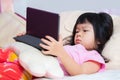 Cute Asian girl is lying down watching cartoon with black tablet. Little kid learn online with touch screen. Royalty Free Stock Photo