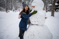 Cute asian girl makes a snowman in winter park.
