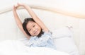 Cute asian girl in pajamas is sitting on bed stretching. Royalty Free Stock Photo