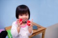 Cute Asian girl playing with orange-red square blocks wooden. Mobile phones placed on wooden tables. Light blue background.