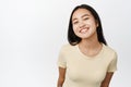 Cute asian girl showing white healthy smile, grinning and looking happy at camera, standing over white background Royalty Free Stock Photo