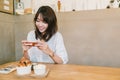 Cute Asian girl taking photo of dessert at coffee shop. Leisure activity or mobile phone photography, food photo concept. Royalty Free Stock Photo