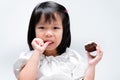 Cute Asian girl tasting cream cake stuck on her finger. Child sucks her finger while holding bakery with her other hand Royalty Free Stock Photo