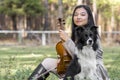 Cute asian girl with a violin withe her dog on the grass on blurred woods background Royalty Free Stock Photo