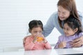 Cute Asian little child girl drinking orange juice from glass while older sister and mother looking and cheers up. Middle aged mom Royalty Free Stock Photo