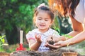 Cute asian little child girl and parent planting young seedlings in the black soil together in the garden
