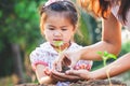 Cute asian little child girl and parent planting young seedlings in the black soil together in the garden