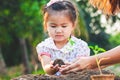 Asian little child girl and parent planting young seedlings in the black soil together in the garden with fun Royalty Free Stock Photo