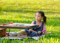 Cute Asian little girl hold magnifier glass and sit near table with colored pencils and toys in the garden with morning light Royalty Free Stock Photo