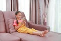 Cute Asian little girl kid playing smartphone on sofa in living room at home Royalty Free Stock Photo