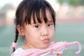 Cute Asian little girl making funny face while took the chin to hold the pink umbrella Royalty Free Stock Photo