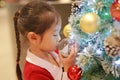 Cute Asian little girl in red dress holding and looking decorative ball of christmas tree in the winter season and happy new year Royalty Free Stock Photo