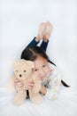 Cute asian little girl and teddy bear doll relaxing with smiling on white bed with looking camera Royalty Free Stock Photo