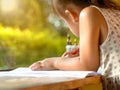 Cute Asian little girl using colored pencils to paint on paper, sitting at a table by the window in the house. Preschoolers study Royalty Free Stock Photo