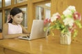 A cute Asian schoolgirl is using a laptop to study online in the living room