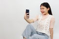 Cute asian teenage smiling, cheerful, sitting and using a smartphone on a white background.