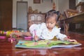 Cute Asian toddler girl child lying on her stomach while coloring with crayons in crafts book with sticker at home, Stay home Stay Royalty Free Stock Photo