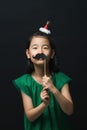 Cute asian woman child with fake mustache and christmas head decoration on black background Royalty Free Stock Photo