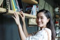 A cute Asian woman choose a book on the bookshelf for reading and she smiled happy on her holiday at home