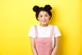 Cute asian woman with makeup and summer clothes, smiling silly and happy at camera, yellow background