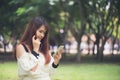 Cute asian woman is reading pleasant text message on mobile phone while sitting in park in warm spring day