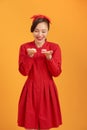 Cute Asian woman in red dress holding macaron over orange background