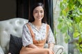 Cute Asian woman sits on the sofa or chair and looks at the camera and smiles happy in portraits at home during relax time