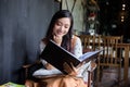 A cute Asian woman is sitting reading a book on the sofa or a chair happy smiling at home during relax time Royalty Free Stock Photo