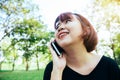 Cute asian woman smiles and talking on mobile phone while sitting in park spring day.