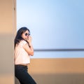 Cute Asian woman stands up against the wall and wears blue sunglasses at rooftop of the building in sunset time Royalty Free Stock Photo