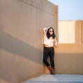 A cute Asian woman stands up and raise elbow up against the wall and wears blue sunglasses at the rooftop of the building at Royalty Free Stock Photo