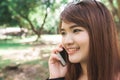 Cute asian woman is talking on mobile phone while sitting in park in warm spring day