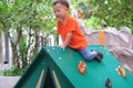 Cute Asian toddler boy having fun trying to climb on artificial boulders at playground on nature