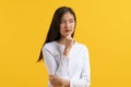 Cute asian young woman in white casual shirt looking up and thinking / imagination isolated on yellow background in studio Royalty Free Stock Photo