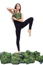 Cute athletic girl holds large head of fresh broccoli in front of her and practices yoga