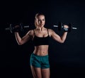 Cute athletic model girl in sportswear with dumbbells in studio against black background. Ideal female sports figure. Royalty Free Stock Photo