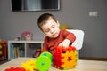 A cute attentive little toddler boy of two years old sits at a children\'s table and plays with multi-colored sorter.