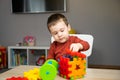 A cute attentive little toddler boy of two years old sits at a children\'s table and plays with multi-colored sorter.