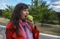 Cute attractive brunette girl in red coat eat green apple fruit on nature background Royalty Free Stock Photo